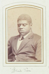 Thomas Greene Bethune, known as Blind Tom, ca. 1870. Black & white photograph. 4 x 2.5 in. Picture depicts the carte-de-visite portrait photograph of musician Thomas Greene Bethune, later Wiggins, known as Blind Tom. Shows the young African American man from his waist up, his body slightly angled to the viewer’s right. His tightly curled hair is shortly cropped. His eyes are closed. He wears a white shirt with a turned down collar. Under the collar is a dark cross tie. He also wears a dark jacket with wide notch lapels, several creases around the waist, and the top button fastened. The photograph is framed within a rectangular shape printed with a thick gold line surrounded by a thin black line. The frame is on light-colored paper. The top edge of the frame is slightly rounded. Hand written text below the portrait reads: “Blind Tom” [End of description]