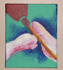 Picture shows a close-up of the tips of Millett-Gallant’s shortened arms – her hands – holding a brown paint brush. Her arms are pink with red overtones. In the right, the paint brush lies vertically down Millet-Gallant’s right, rounded-tipped hand, angled slightly left. Her left hand resembling a closed fist rests perpendicular to the brush and her right hand. Her two touching hands form an inverted V-shape. In the upper left corner is a half of a brown egg-shaped object. It is situated above the tip of the paint brush. The background is green with blue shading enclosing Millett-Gallant’s hands. [end of description]