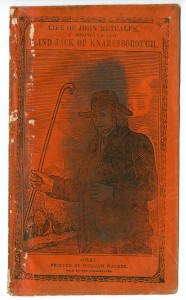 Picture shows the illustrated orange paper cover of a booklet. The illustration fills most of the cover and shows a three-quarter length engraved portrait of a man, presumably John Metcalfe. The man stands, his eyes closed, and faces slightly away from the viewer. He holds a staff in his right hand. Both of his arms are bent at the elbow, in an L-shape, and rest at the side of his body. He is attired in 18th-century clothing. He wears a dark-colored slightly floppy hat, a white cravat, and a dark-colored vest under a dark-colored overcoat with wide collars and wide hip pockets. Engraved lines resembling scratch marks give the man’s hat and clothing texture. In the far left background is a cluster of trees. Above the man are multiple rows of horizontal parallel lines with two unlined areas forming the shapes of clouds. A black-colored stain runs vertically down the center of the image, slightly obscuring the portrait. The title text “Life of John Metcalfe. [next line] Commonly Called [next line] Blind Jack of Knaresborough,” sits above the illustration and in the upper edge of the cover. Below the illustration is the text of the imprint: Otley: [next line] Printed by William Walker. [next line] Sold by the Bookseller. A rectangular-shaped border comprised of inter-twirled lines surrounds the illustration, title and imprint. [End of description]