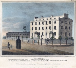 Picture shows a four-story rectangular building with many rectangular windows. The building includes two front entrances with porticos. The structure is white, and its front is lit by sunlight. Pedestrians – eight total with six men, two women and one boy – walk on the sidewalk in front of and across from the building. Small trees evenly line the sidewalk in front and to the left of the building. A dark-colored watchman’s guardhouse, shaped like a chimney, stands across the street from the building. A man with a cane, and a boy, holding his hand, walk past the guardhouse. The boy appears to be gesturing in the direction of the guardhouse and the building. Text printed below the images reads: “Lith. Of J. T. Bowen, Phila. Pennsylvania Institution for the Instruction of the Blind. Published by J.T. Bowen at his Lithographic & Print Colouring Establishment, 94, Walnut St Philada. Entered according to act of Congress in the year 1840 by J. T. Bowen in the Clerk’s Office of the Dt. Ct. for the En. Dt. of Pa.[End of description]